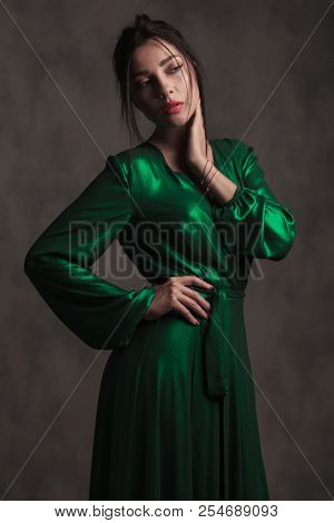 portrait of sensual woman in a green silk dress looking to side while standing on white background and holding her neck