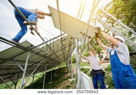 Stand-alone Solar Photo Voltaic Panel System Installing. View From Below Of Three Technicians Worker