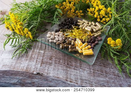 Ayurvedic Herbal Pills On The Glass Plate And Tansy Yellow Flowering Plant. Healthy Life Concept