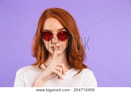Portrait of a pretty young girl standing isolated over violet background, showing silence gesture