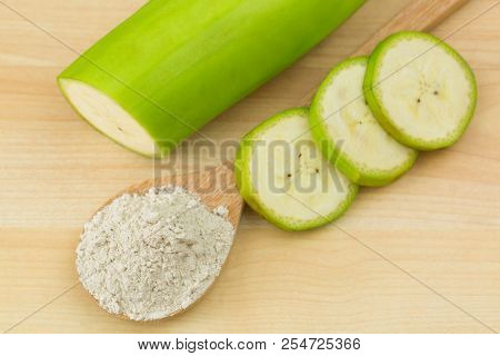 Synbiotic dried banana powder next to sliced fruit of organic whole Gros Michel banana, known as Big Mike, top view on wooden background 