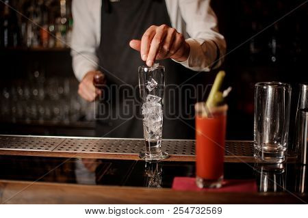 Bartenter Adding Ice Into An Empty Cocktail Glass On The Blurred Foreground Of Bloody Mary Cocktail