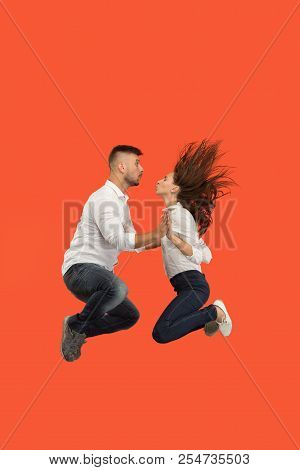Freedom In Moving. The Happy Young Couple Jumping And Gesturing Against Red Studio Background. Runni