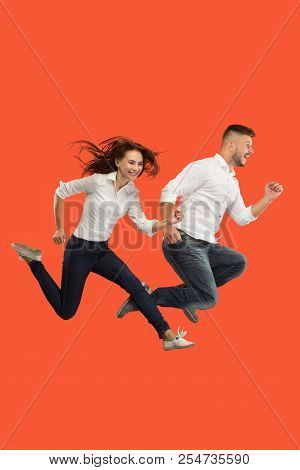 Freedom In Moving. The Happy Young Couple Jumping And Gesturing Against Red Studio Background. Runni