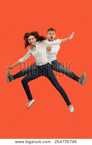 Freedom In Moving. The Happy Young Couple Jumping And Gesturing Against Red Studio Background. Runni