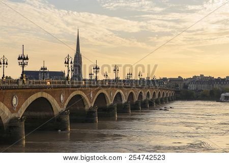 Pont De Pierre Stone Bridge On The River Garonne In Bordeaux, France At Sunset With The St Michel Ch