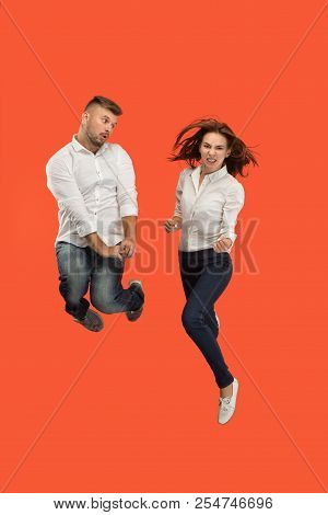 The Man And Angry Woman Jumping Against Red Studio Background. Runnin Girl And Man In Motion Or Move