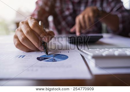 Close Up Of Businessman Point The Pen On Graph Of The Business Data Financial Report And Using Calcu