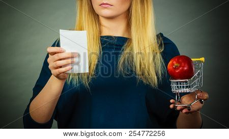 Worried Woman Holding Shopping Basket With Fruits Looking At Bill Receipt Being Scared Of Huge Price
