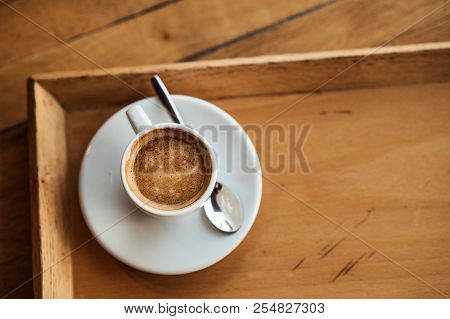 Top View Of White Cup With Black Coffee On A White Saucer And Teaspoon On Brown Wooden Background Wi