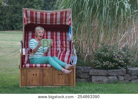 The Young Woman In The Roofed Wicker Beach Chair Is Happy About The Great Shopping On The Internet