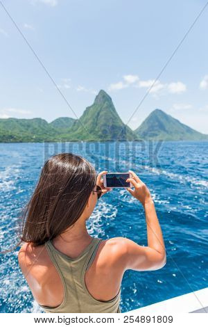 Caribbean travel girl taking photo with phone on St Lucia Pitons boat cruise ride in tropical vacation summer lifestyle.