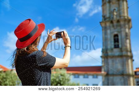 Young girl in red hat with smartphone in hands take photos of ancient tower uring travel in Lisbon, Portugal.