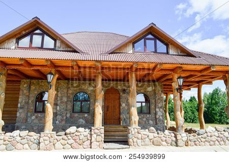 A Large Wooden Hut House In The Woods Of Logs Of Planks And Stone With Columns Of Tree Trunks With A