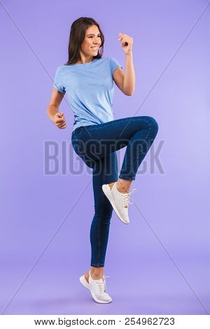 Full length portrait of a cheerful young woman celebrating success isolated over violet background
