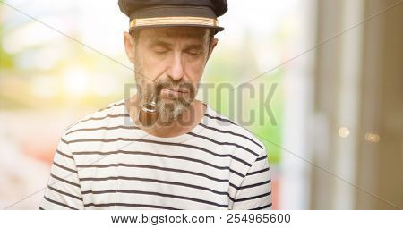 Sailor captain man smoking a tobacco pipe with sleepy expression, being overworked and tired