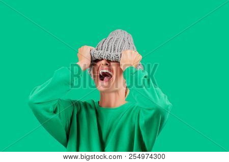 Furious. Emotional Angry Woman Is Pulling Wool Hat Over Her Eyes On Green Background