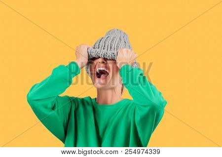 Furious. Emotional Angry Woman Is Pulling Wool Hat Over Her Eyes On Yellow Background