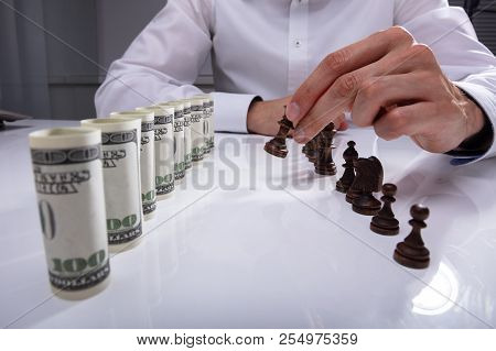 Businessperson Making First Move With Chess Piece Against Rolled Up Banknotes