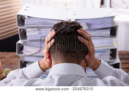 Close-up Of Stressed Businessman With Hand On Head In Front Of Stacked Folders