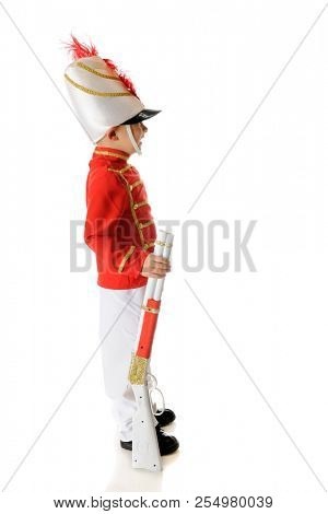 Profile of a preschool Christmas soldier standing eret with his gun by his side.  On a white background.