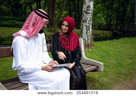 Young Beautiful Arabian Couple Casual And Hijab, Abaya, Taking A Selfie On The Lawn In Summer Park.