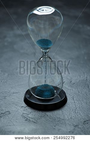 Image of hourglass with blue sand on black background