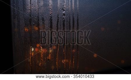 Close-up Of Window With Raindrops On Blurred Background Of Lights. Concept. Dim Lights Shine Through