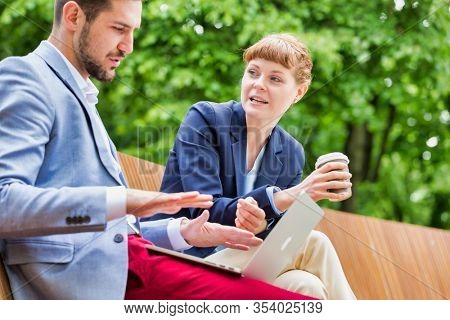 Businessman discussing plans over laptop with beautiful businesswoman while sitting on bench