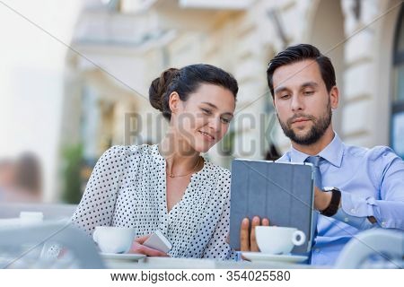 Businessman discussing plans over digital tablet to businesswoman while sitting and waiting for their food at restaurant