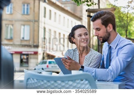 Businessman discussing plans over digital tablet to businesswoman while sitting and waiting for their food at restaurant