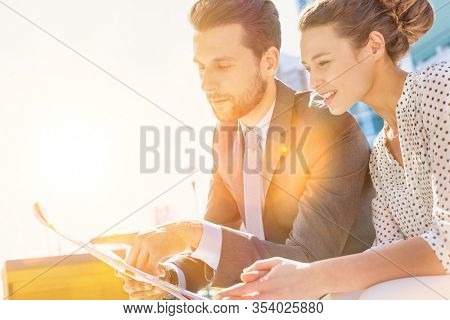 Young attractive businessman discussing business plans over document with beautiful businesswoman while sitting on bench against office building