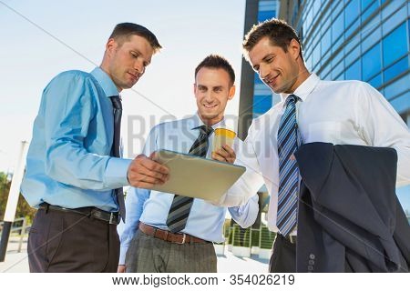 Mature attractive businessman showing and discussing plans over digital tablet with colleagues against office building