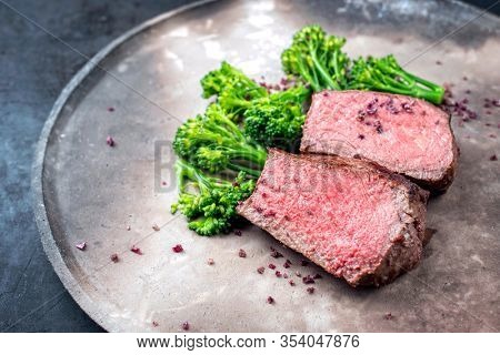 Barbecue dry aged wagyu roast beef natural sliced offered with rapini and salt as top view on a modern design plate with copy space left 