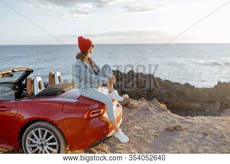 Woman Enjoying Beautiful View On The Ocean, Sitting On The Convertible Car On The Rocky Coast During