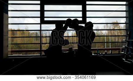 Two Male Boxers Training In The Dark Gym Near The Window With Daylight. Side View Of Two Fighters, A