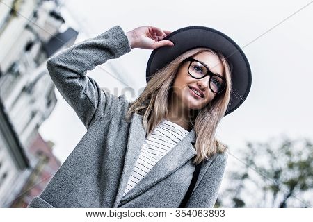 Happy Gentle Hipster Girl In Modern Urban Clothing Posing On City Street. Young And Fashionable Woma