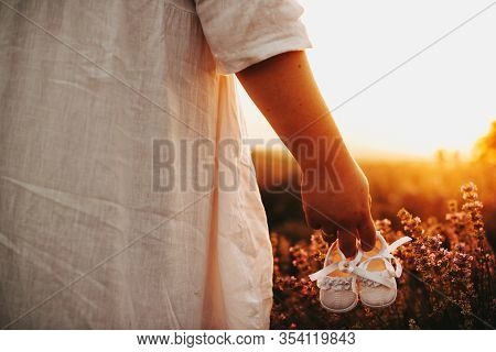 Caucasian Woman Dressed In A White Dress Is Posing In A Wheat Field While Holding A Pair Of Baby Sho