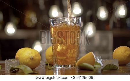 Close Up Tea Pouring Into The Glass With Ice And Lemon. Glass With Iced Tea Or Cocktail, Ice, Lemons