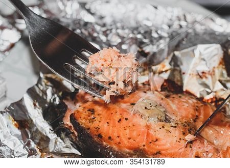 A Steak Of Baked Salmon Is Cut With A Knife And Fork During A Meal.