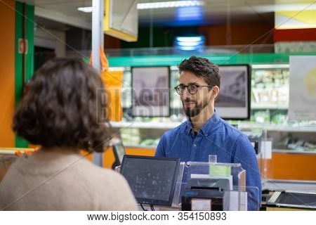 Man And Woman Talking At Pay Desk In Grocery Store. Customer Talking With Cahier While Buying Goods 