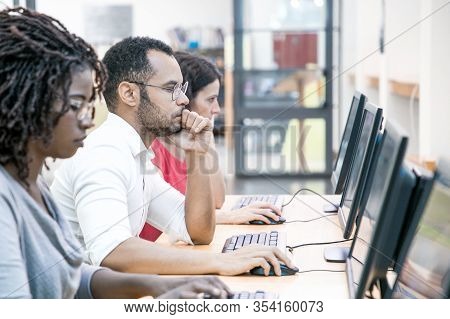 Multiracial Group Of Students Training In Computer Class. Line Of Man And Women In Casual Sitting At