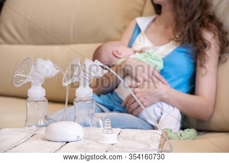 A Young Mother Breastfeeds Her Baby And An Electric Breast Pump Is Standing In Front Of Her On A Woo