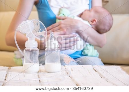 A Young Mother Breastfeeds Her Baby And An Electric Breast Pump Is Standing In Front Of Her On A Woo