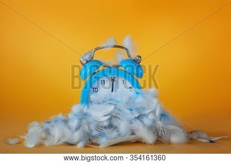 Blue Alarm Clock In A Heap Of Feathers On A Yellow Background