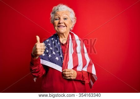 Senior beautiful grey-haired patriotic woman wearing united states flag over red background happy with big smile doing ok sign, thumb up with fingers, excellent sign