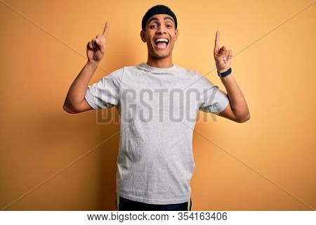 Handsome african american sportsman doing sport wearing sportswear over yellow background smiling amazed and surprised and pointing up with fingers and raised arms.