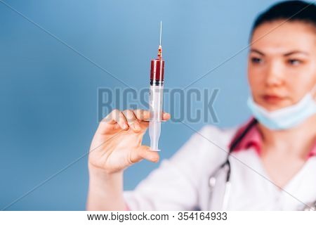 Young Girl Doctor Holding Syringe With Blood In His Hand In A White Coat And Mask On Her Face
