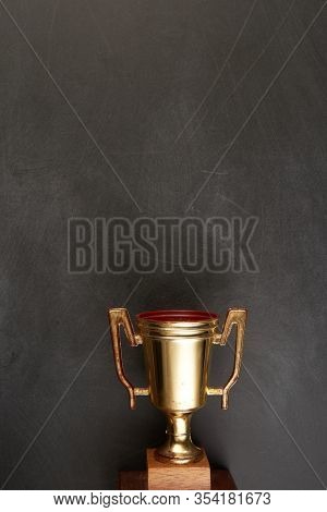 Golden trophy over blackboard background. top view. flat lay.Trophy is a specific achievement, serves as recognition / evidence of merit, awarded for sporting events