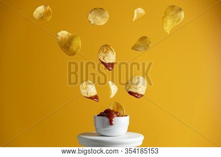 Tasty Potato Chips Falling Into Blow With Tomato Sauce, Frozen In The Air. Yellow Food Art Backgroun